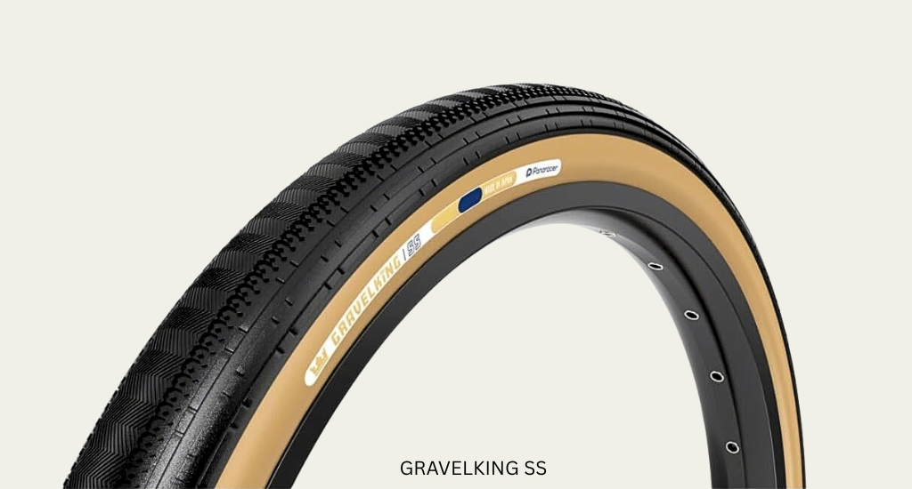 Close-up of a Panaracer GravelKing SS tire with a black semi-slick tread and classic tan sidewalls, mounted on a black rim against a clean, off-white background.